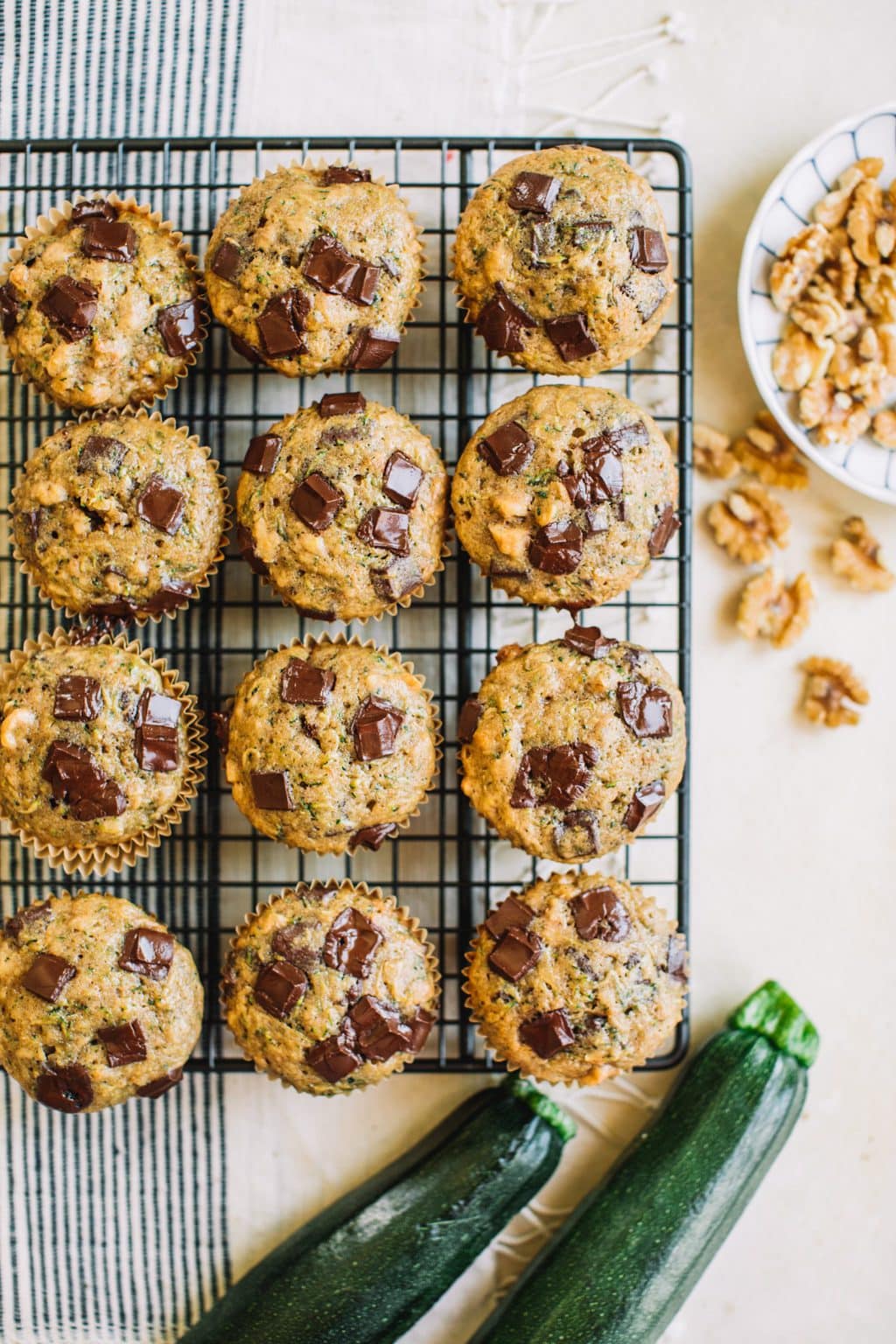 zucchini muffins with chocolate chips in wire rack with fresh zucchini and walnuts