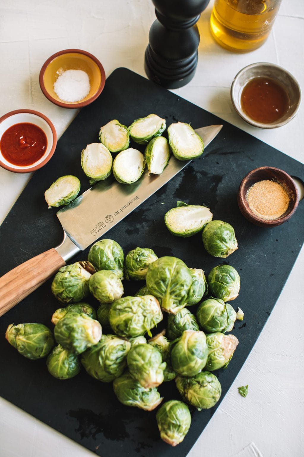 halved and whole brussels sprouts with knife on cutting board with sriracha, salt, garlic powder, honey in small bowls