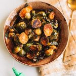 crisp honey sriracha brussels sprouts in brown bowl with gold spoon on the side