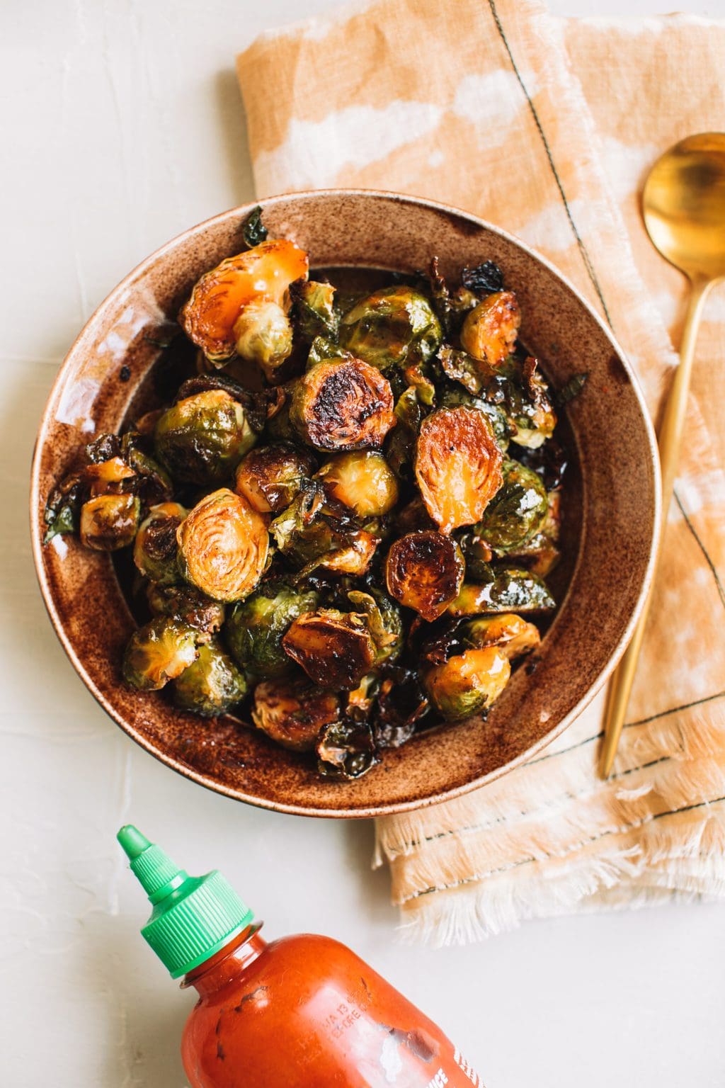 crisp honey sriracha brussels sprouts in brown bowl with gold spoon on the side