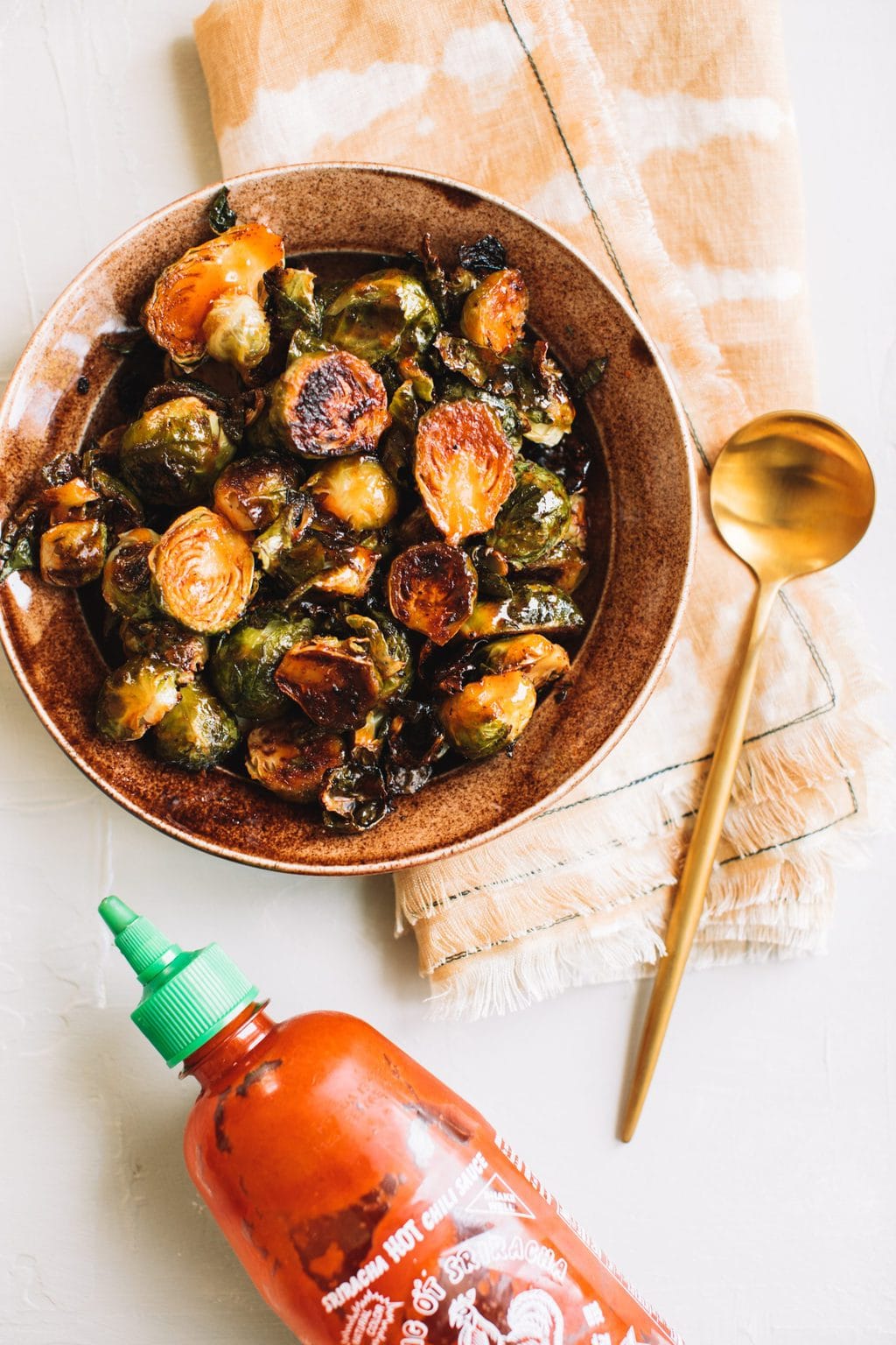 crisp honey sriracha brussels sprouts in brown bowl with gold spoon on the side