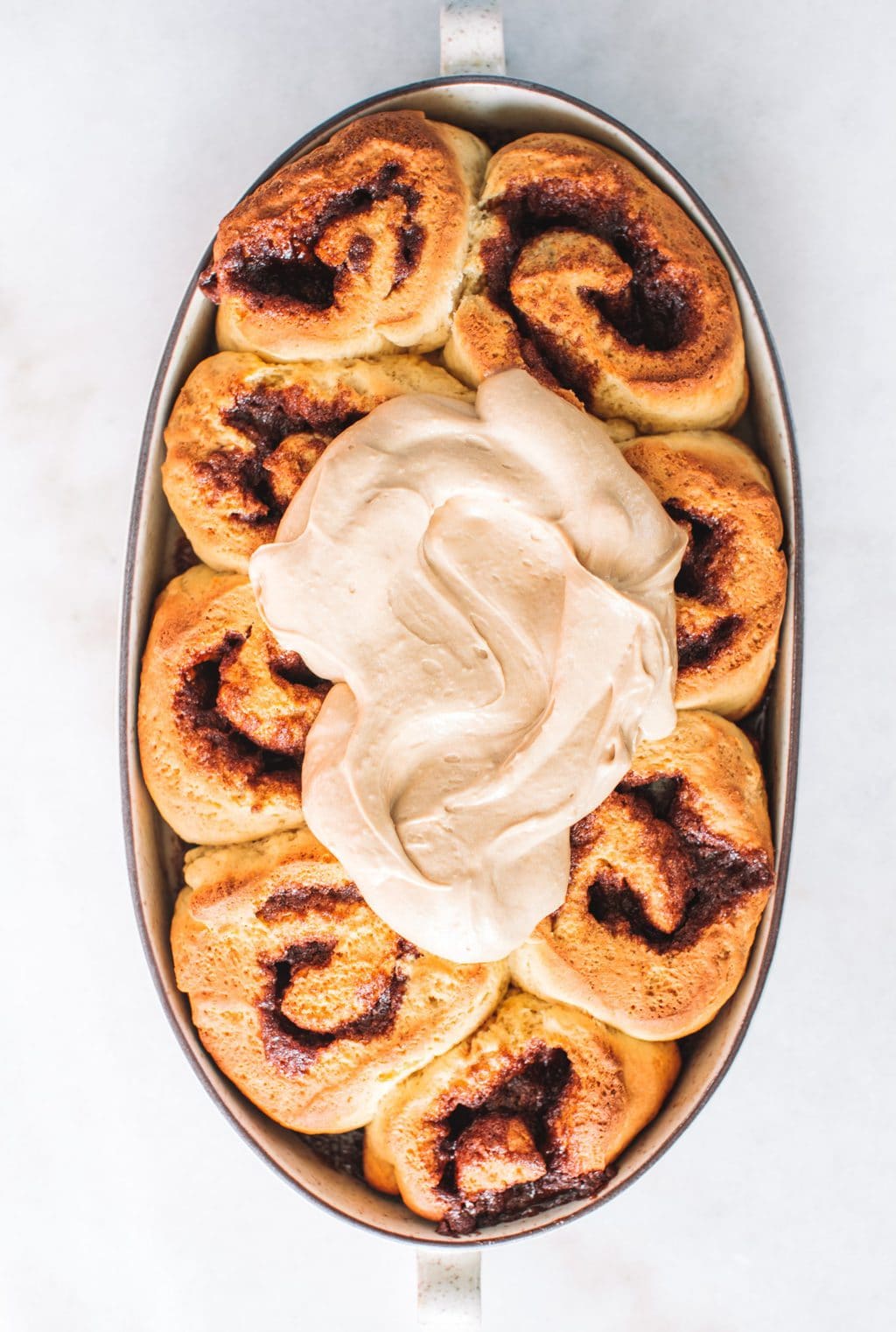 A dish of cinnamon rolls with a large dollop of espresso icing in the middle.