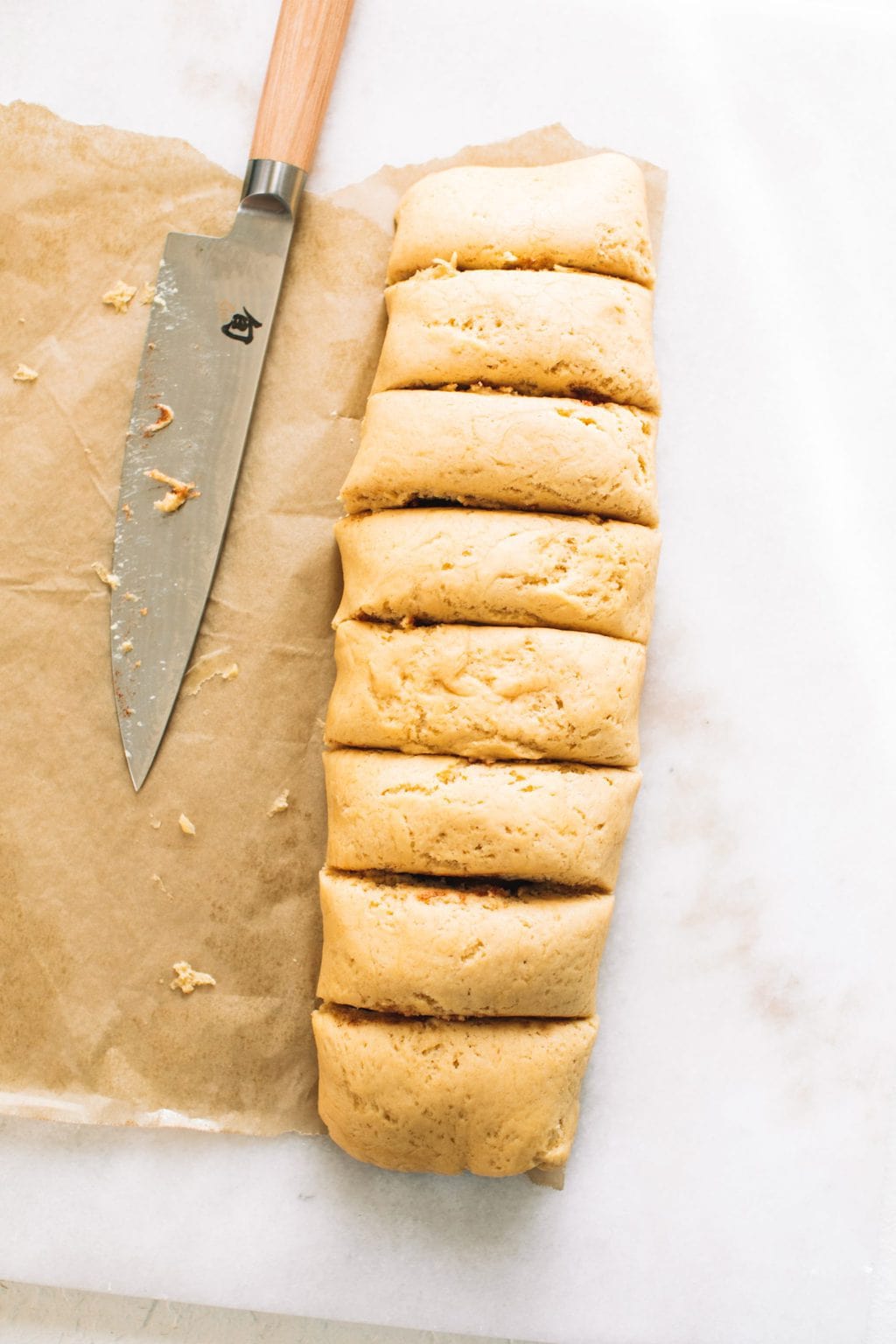 Cinnamon roll loaf cut into rolls on parchment paper next to knife.