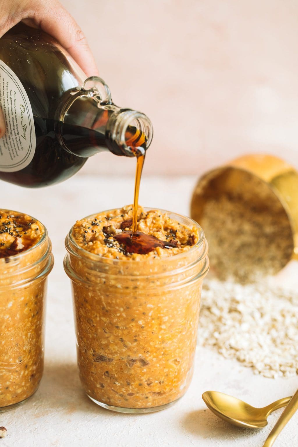 maple syrup being poured on top of pumpkin spice overnight oats in glass jar