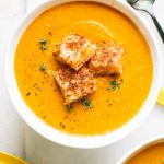 creamy pumpkin soup recipe in white bowl topped with grilled cheese croutons and fresh thyme