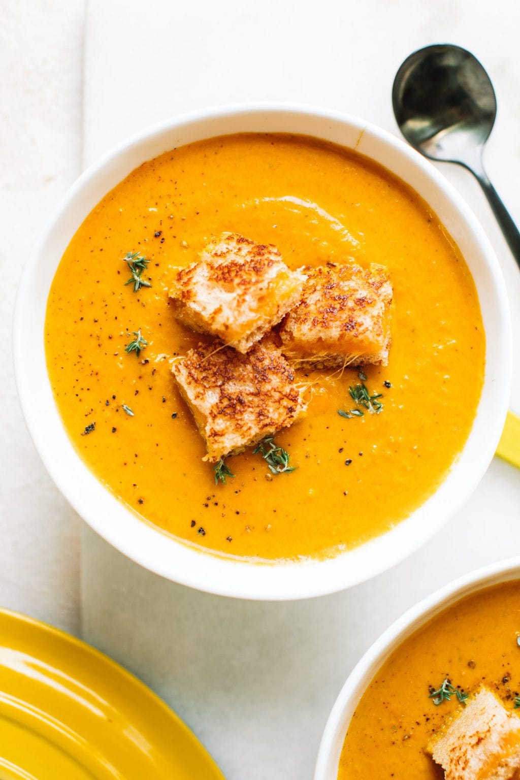 creamy pumpkin soup recipe in white bowl topped with grilled cheese croutons and fresh thyme