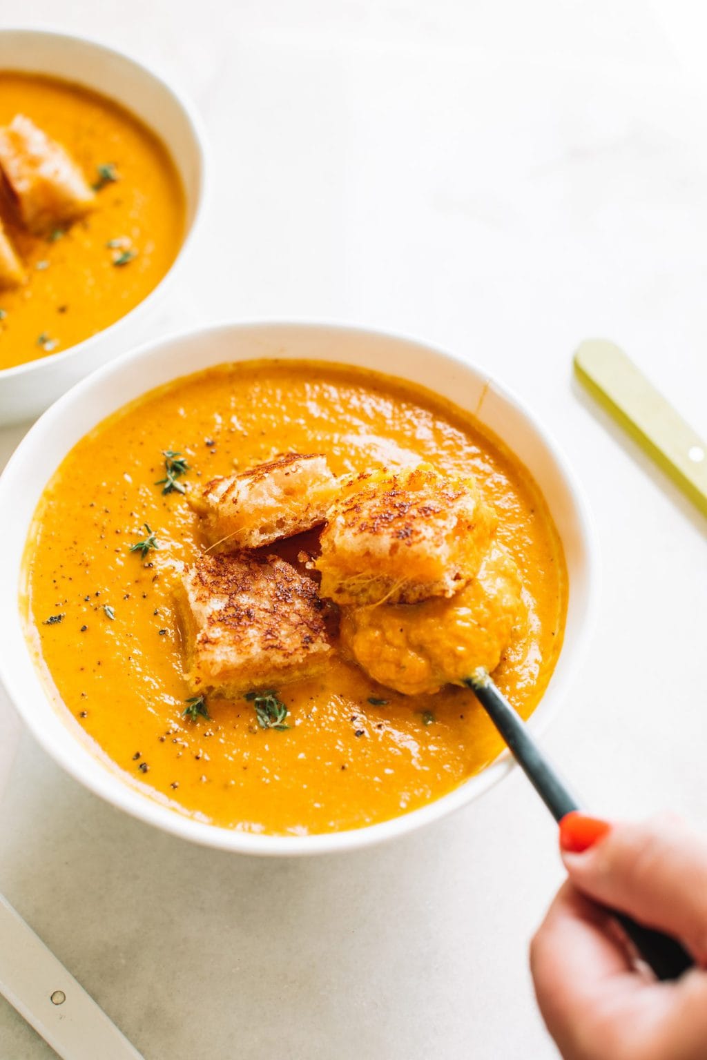 hand stirring spoon in bowl of spicy pumpkin soup with grilled cheese croutons