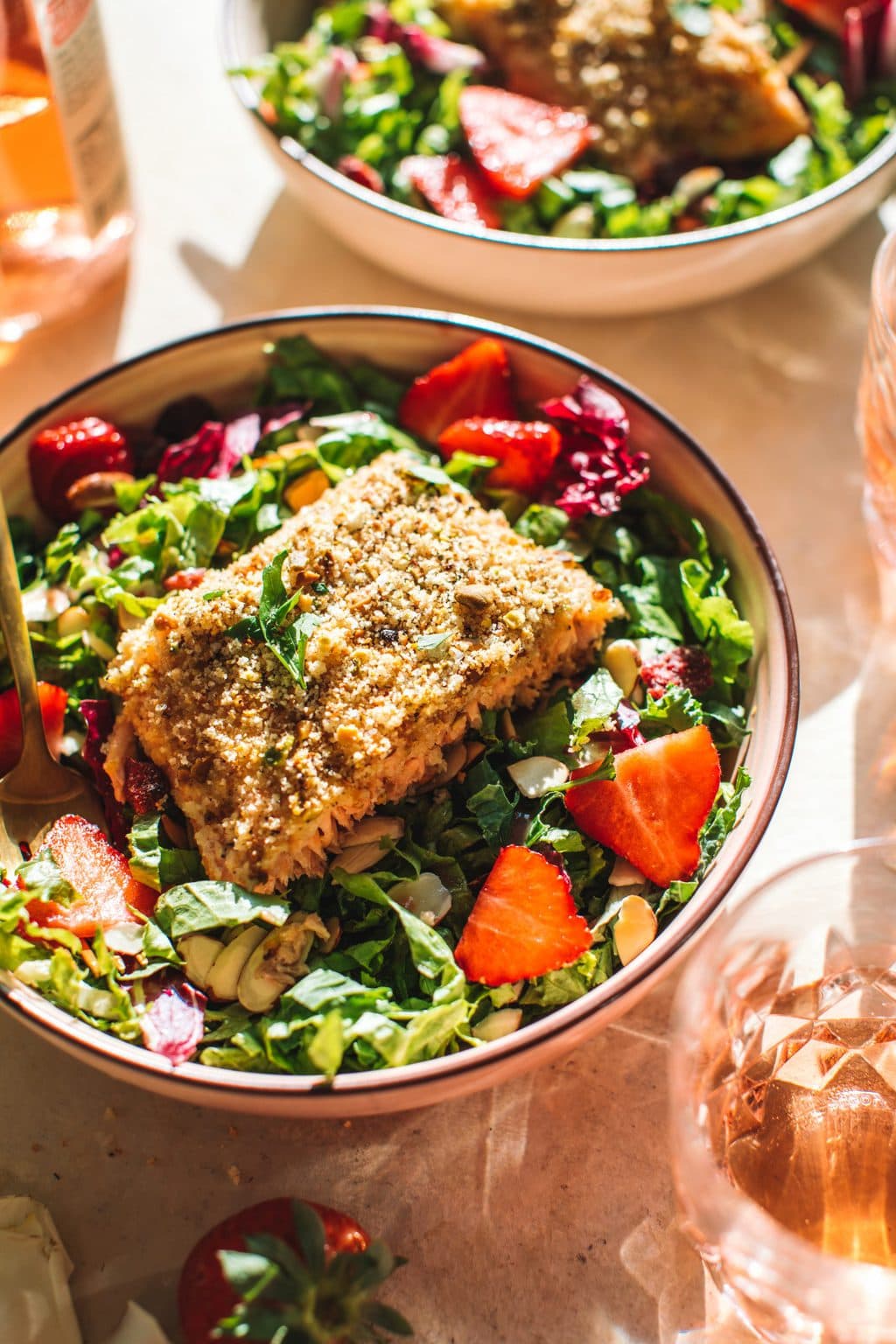 A bowl of salad topped with pistachio crusted salmon. 