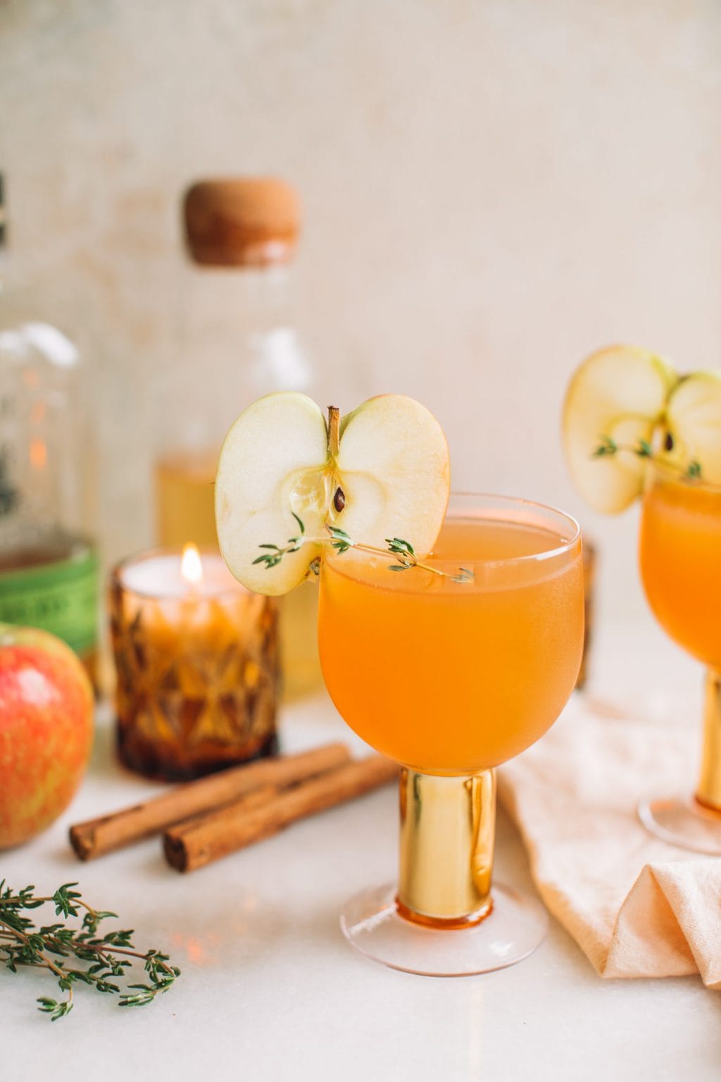 A glass cup with orange liquid and an apple slice garnish.