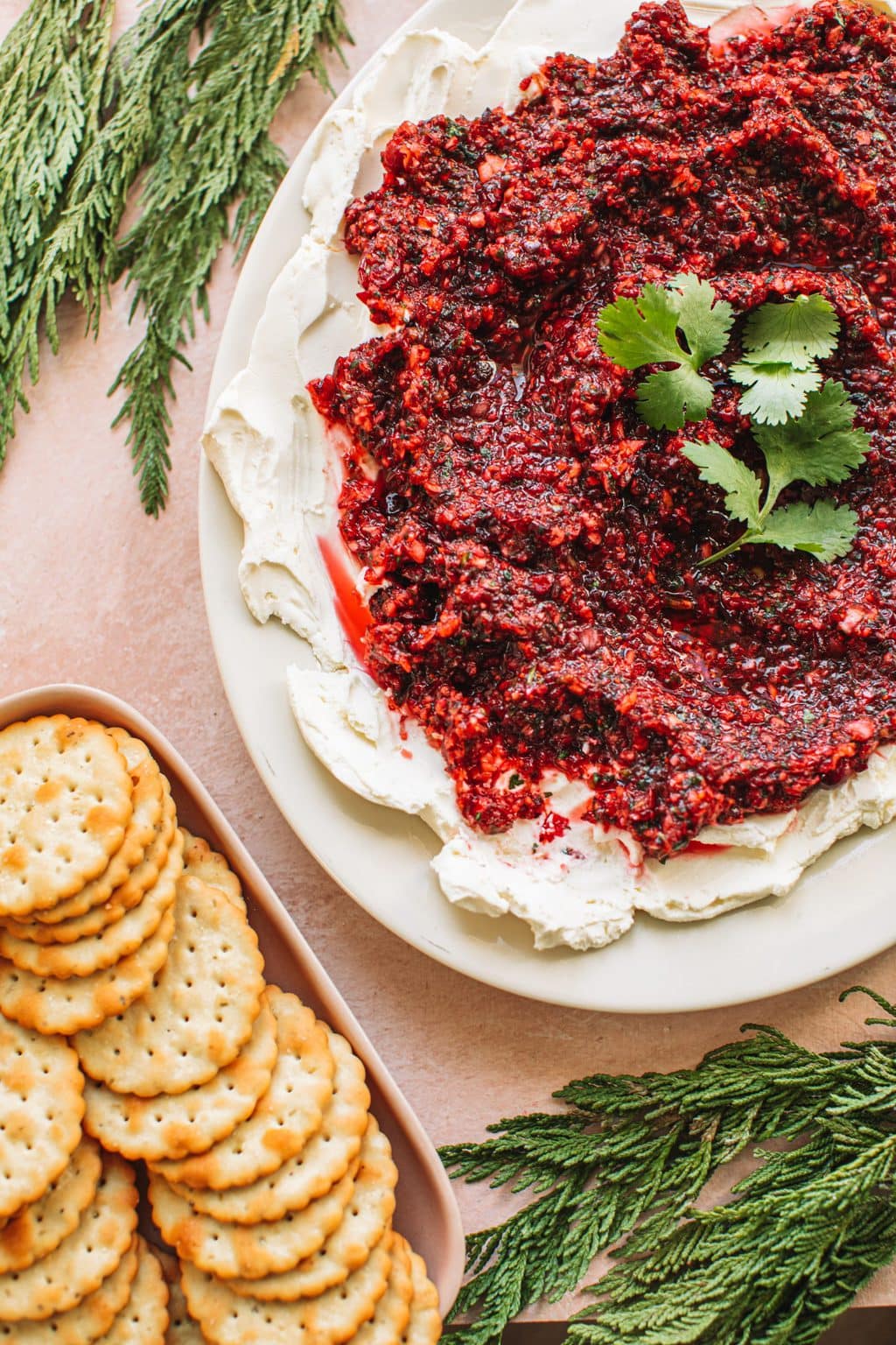 Red jalapeño cranberry dip on top of cream cheese spread on white plate next to dish of crackers