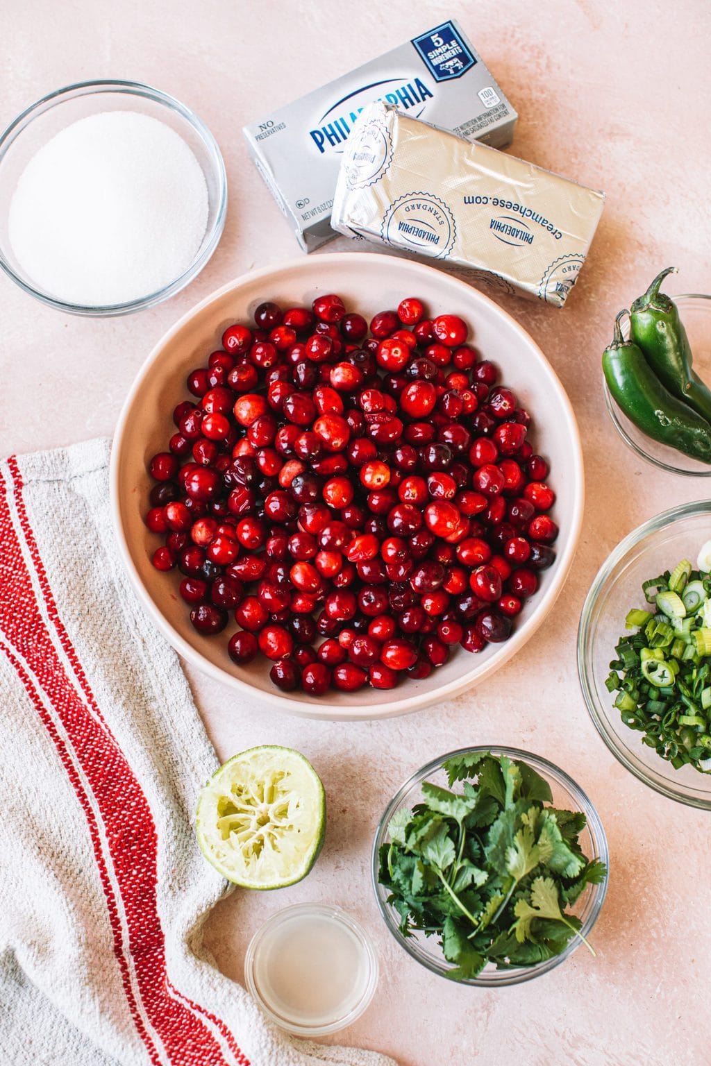 Ingredients top shot, bowl of red cranberries, small bowls of cilantro, jalapeños, chopped onion, and sugar, and two blocks of Philadelphia cream cheese