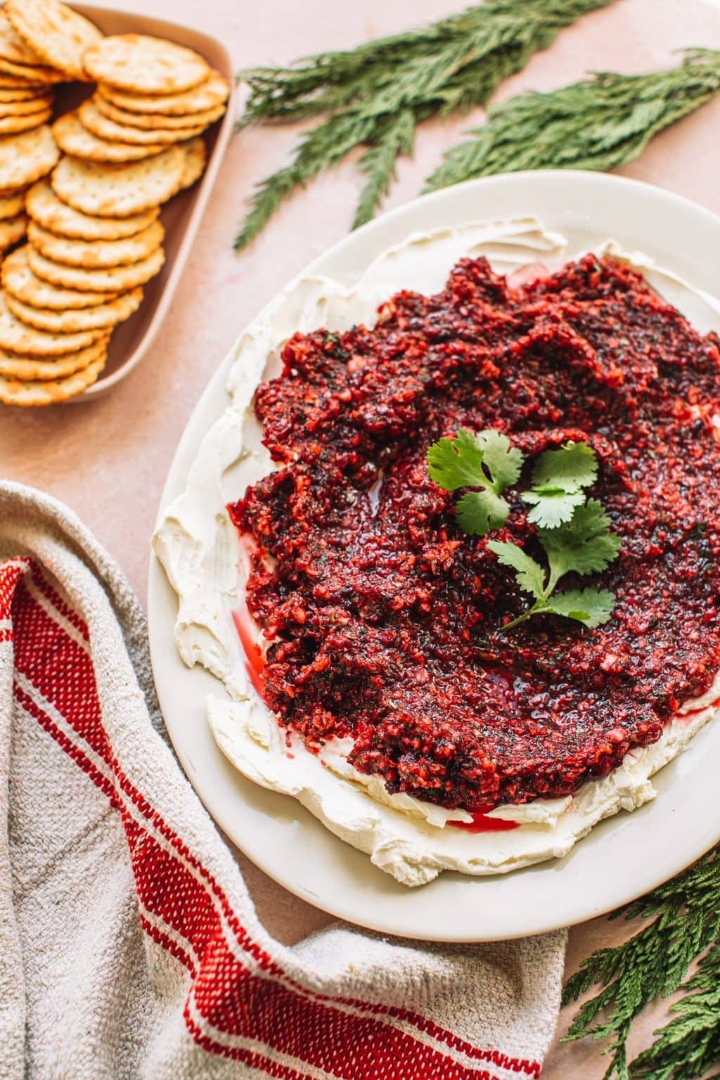 Red jalapeno cranberry dip on top of cream cheese spread on white plate next to dish of crackers