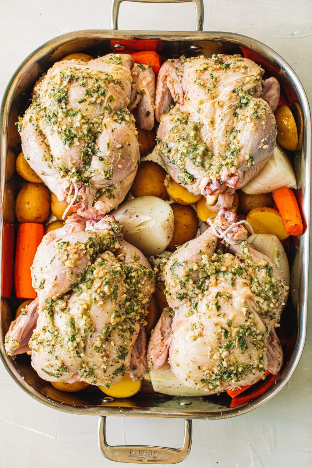 Four cornish hens set on top of carrots, onions and potatoes in a roasting dish before going into the oven