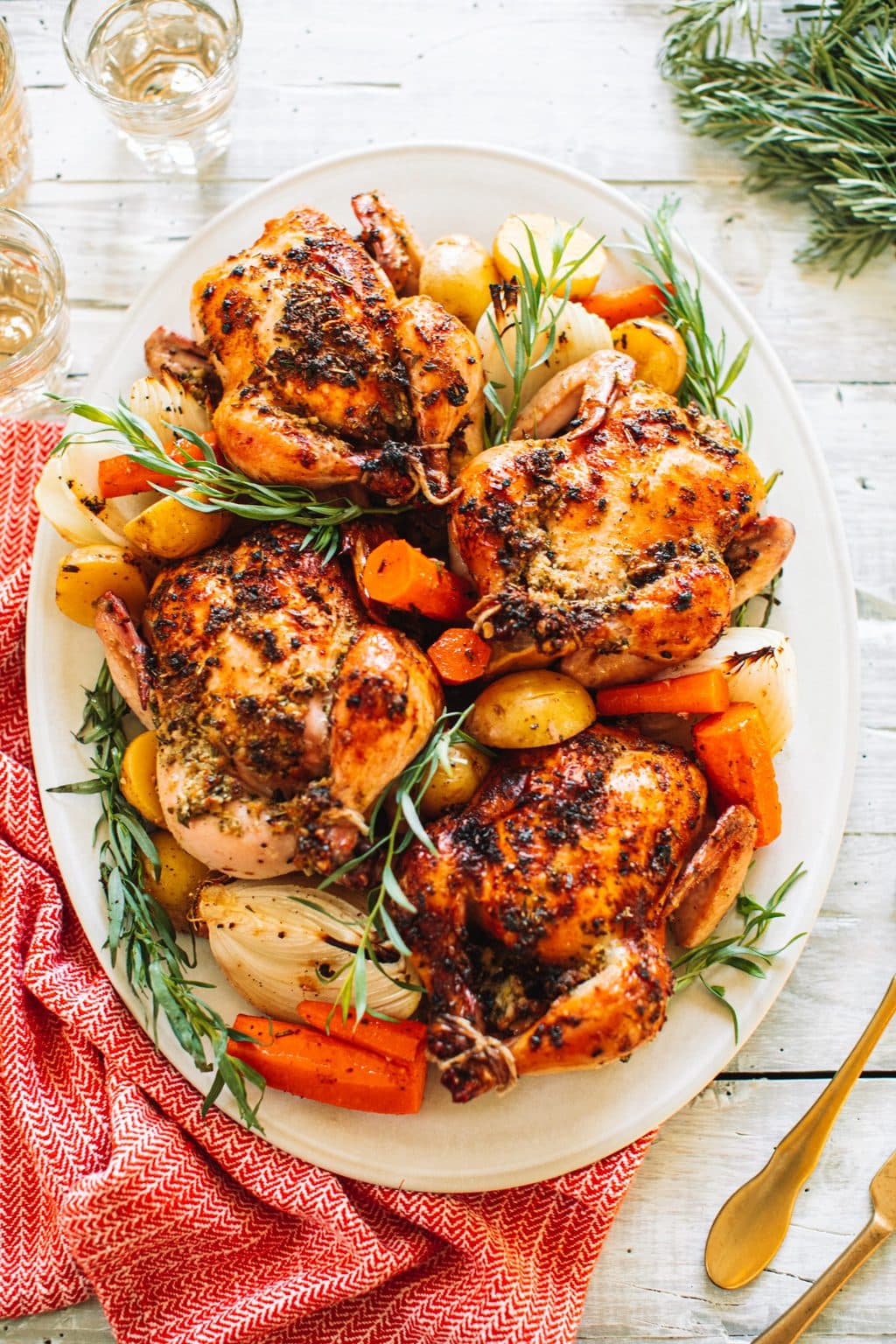 Four oven baked cornish hens arranged on a white plate with carrots, onions and potatoes