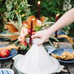 moroccan theme table scape with blue plates, yellow napkins, and a candle set outdoors on a wooden table