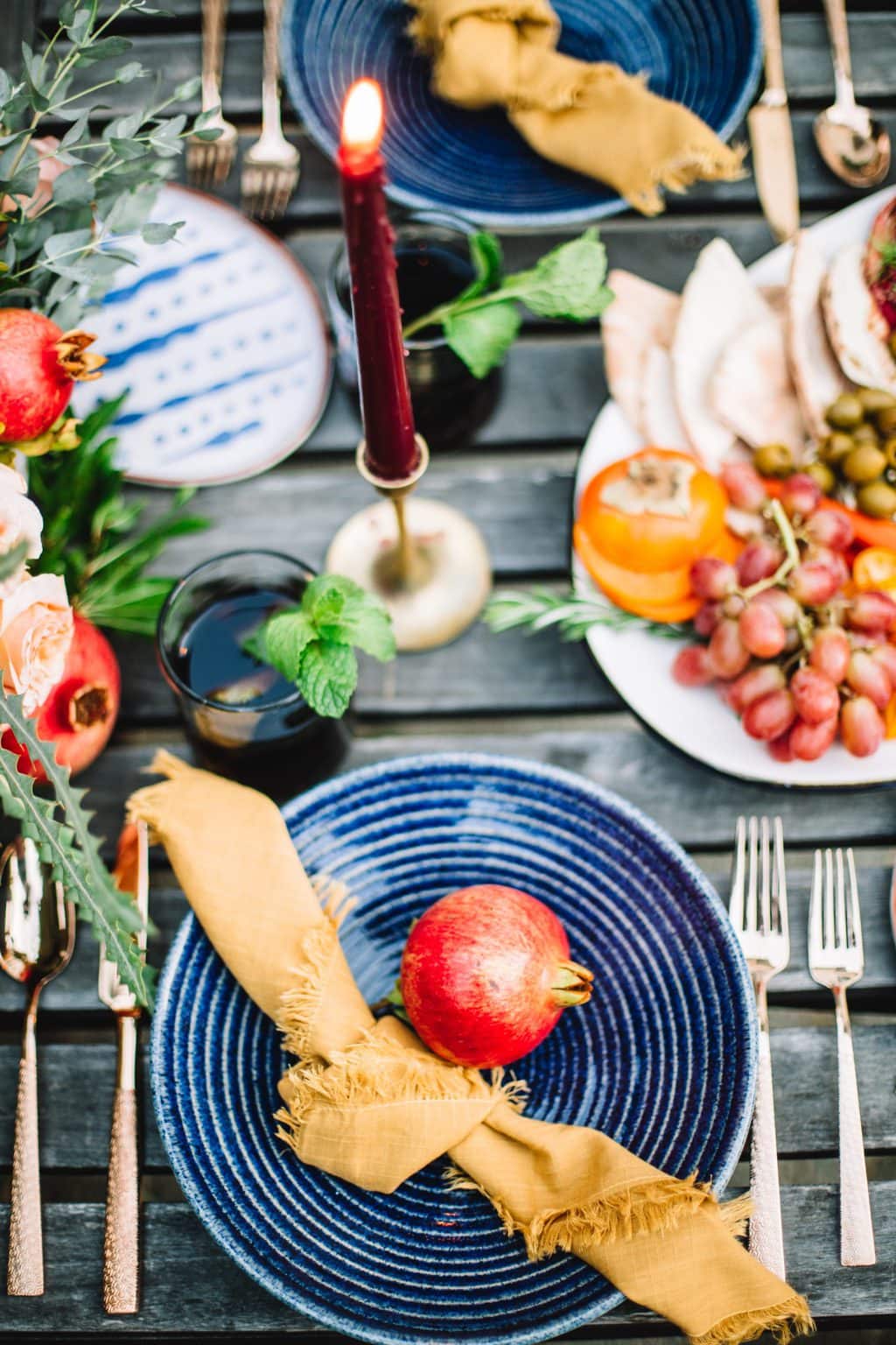 moroccan theme table scape with blue plates, yellow napkins, and a candle set outdoors on a wooden table