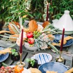 moroccan theme table scape with blue plates, yellow napkins, and a candle set outdoors on a wooden table