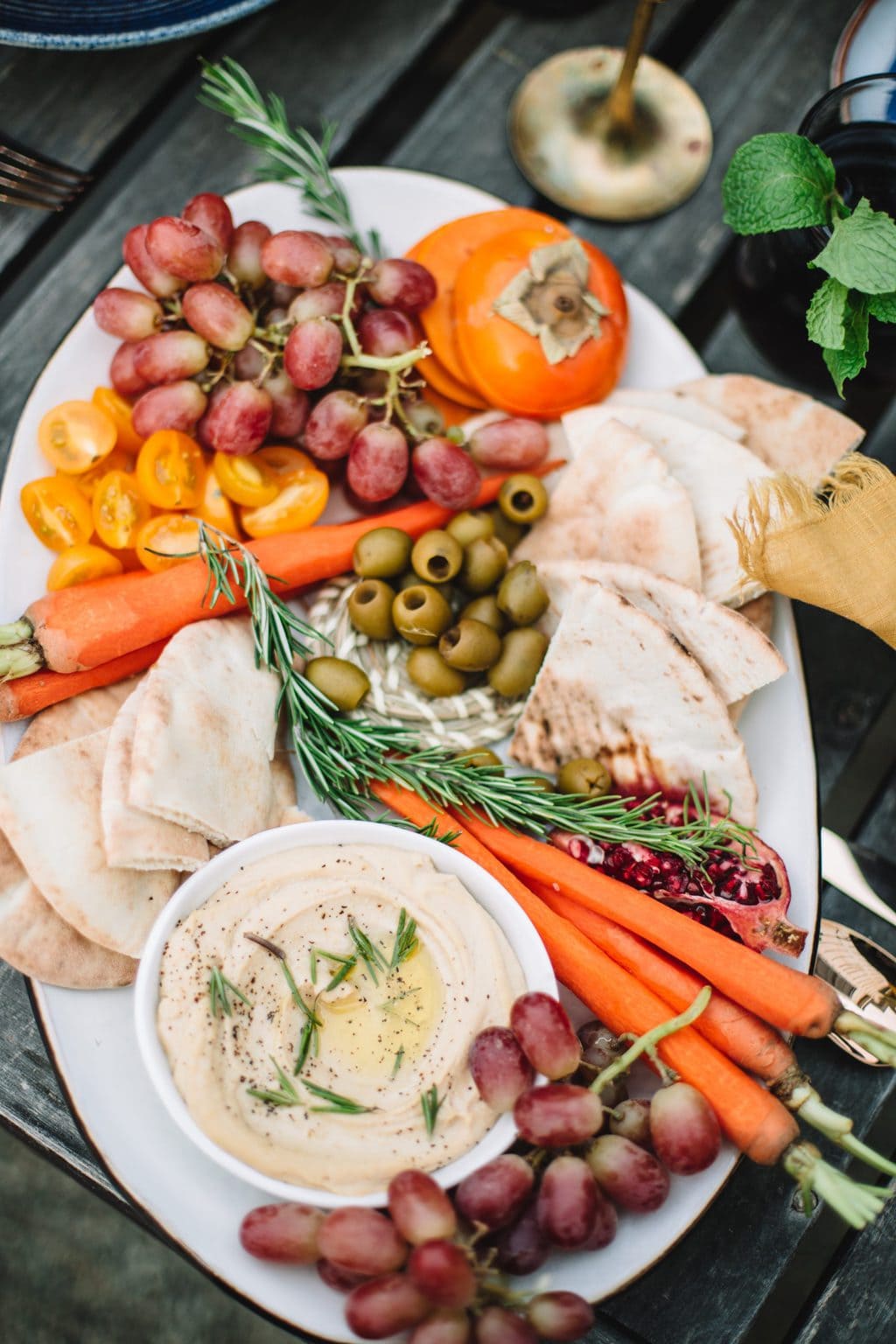 top shot of fruit and vegetable platter with hummus on white plate on wooden table outside