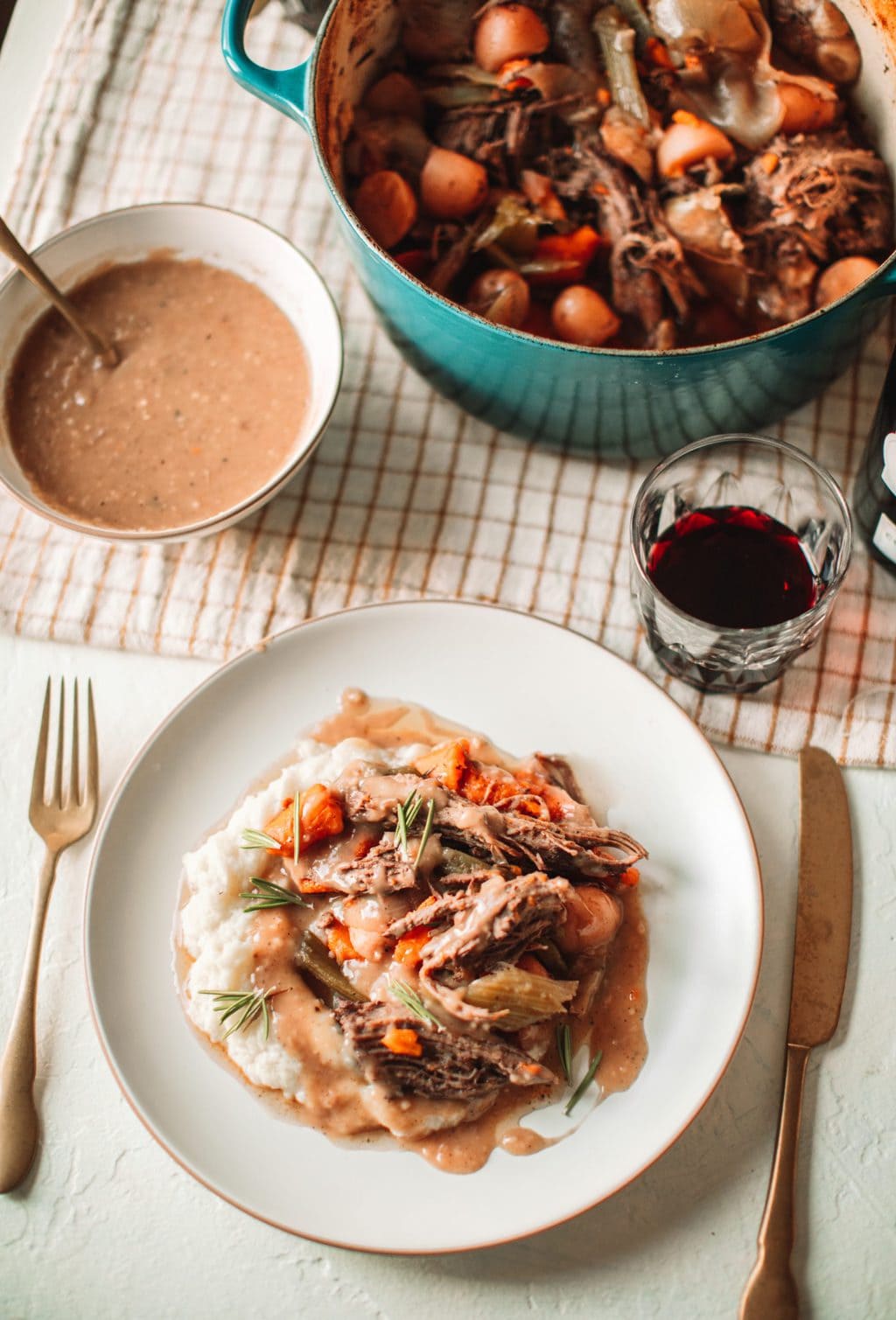 top shot of pot roast and mashed potatoes on white plate next to bowl of gravy