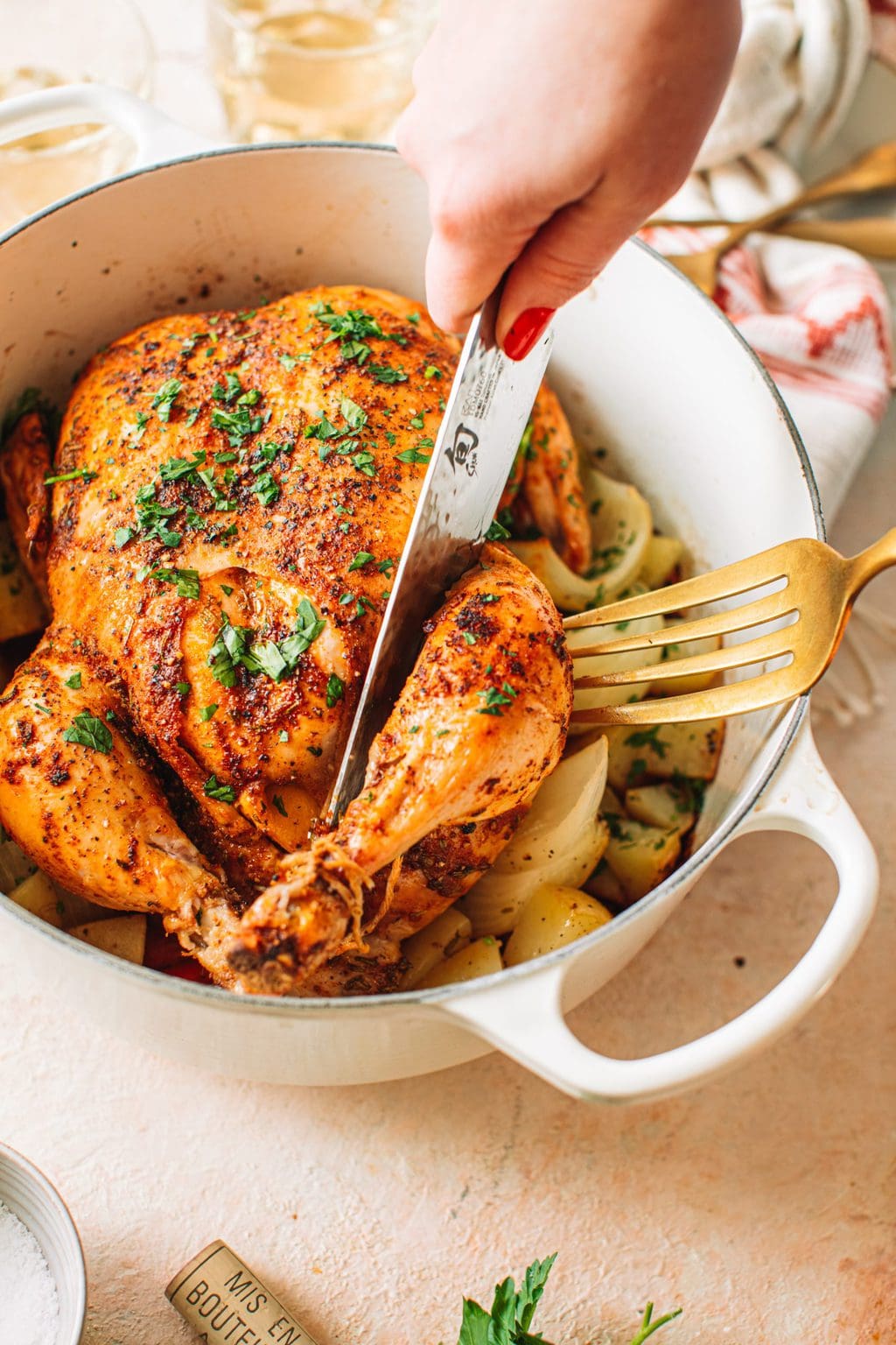 Closeup shot of woman slicing whole chicken that is sitting in Dutch oven.