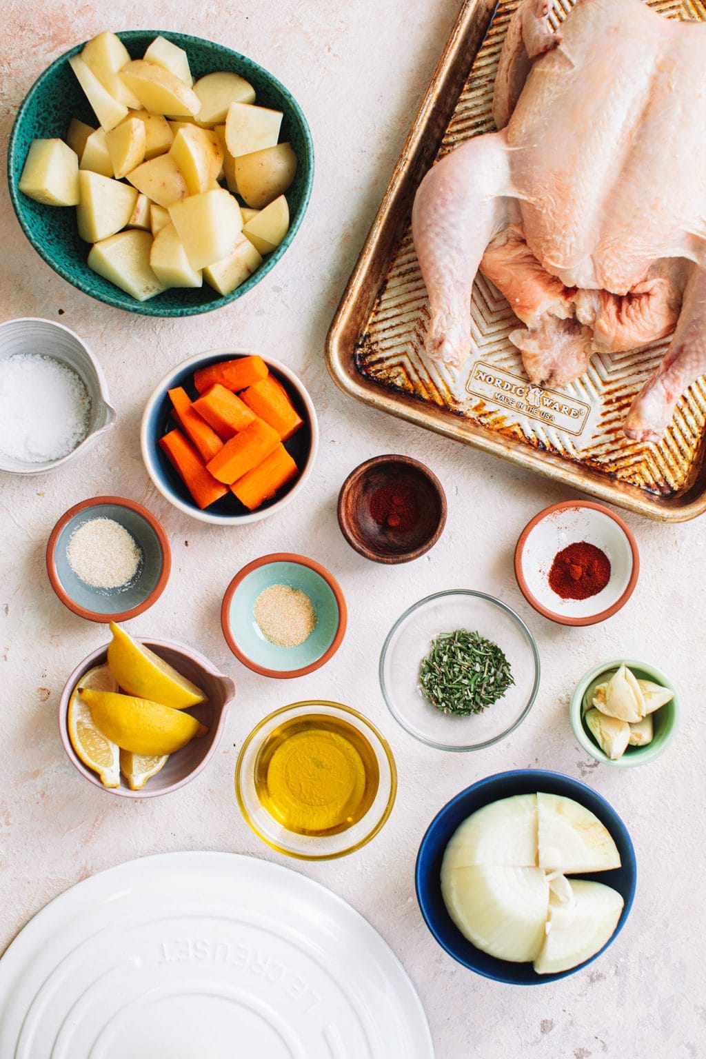 Top shot of sliced vegetables, herbs, and other ingredients in cups next to whole chicken.