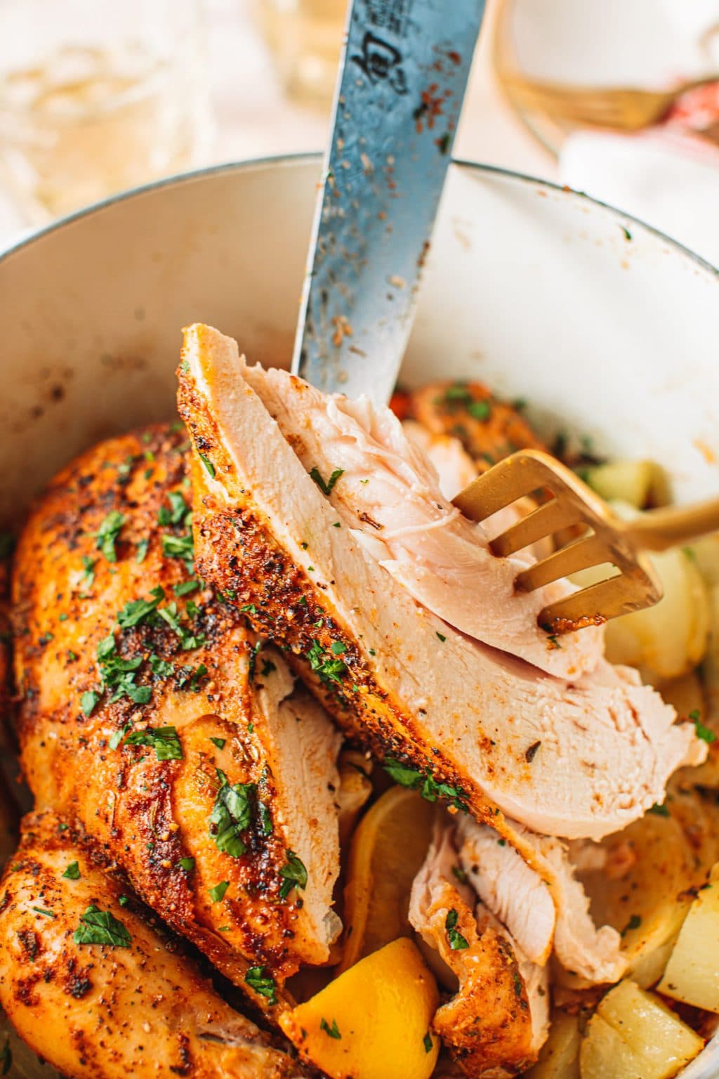 Closeup of sliced piece of roasted chicken held with gold fork.