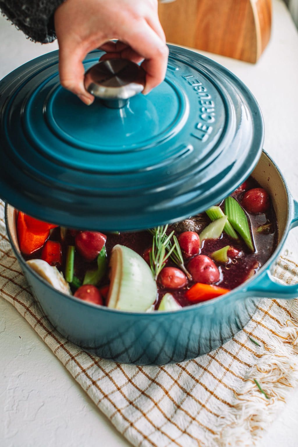 top shot of hand opening blue top to show pot roast and vegetables in light blue dutch oven