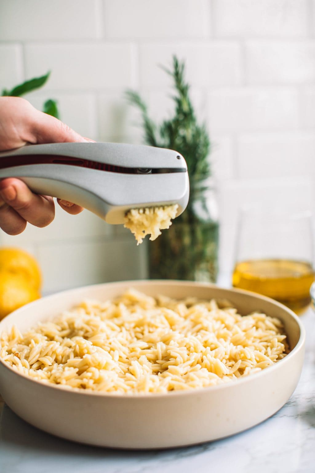 Close up shot of woman squeezing freshly minced garlic onto pasta dish.