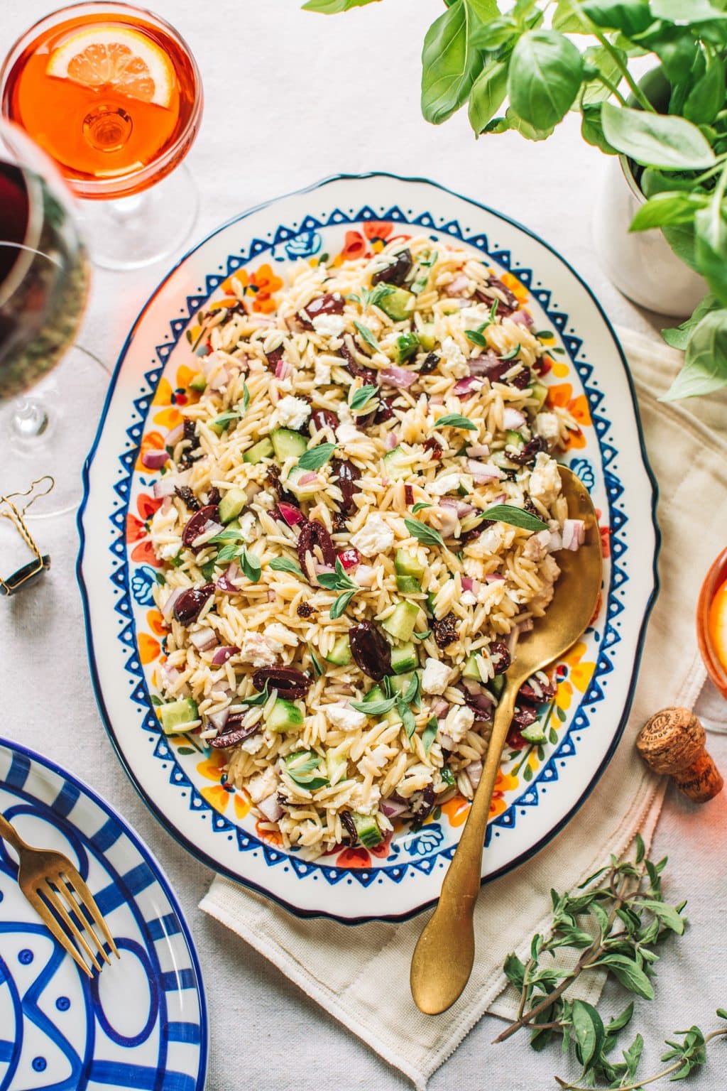 Top shot of greek pasta salad with gold spoon on large oval serving dish.