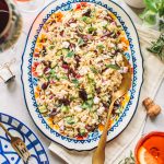 Top shot of greek pasta salad with gold spoon on large oval serving dish.