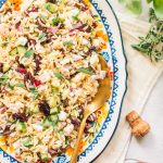 Top shot of greek pasta salad with gold spoon on large oval serving dish.