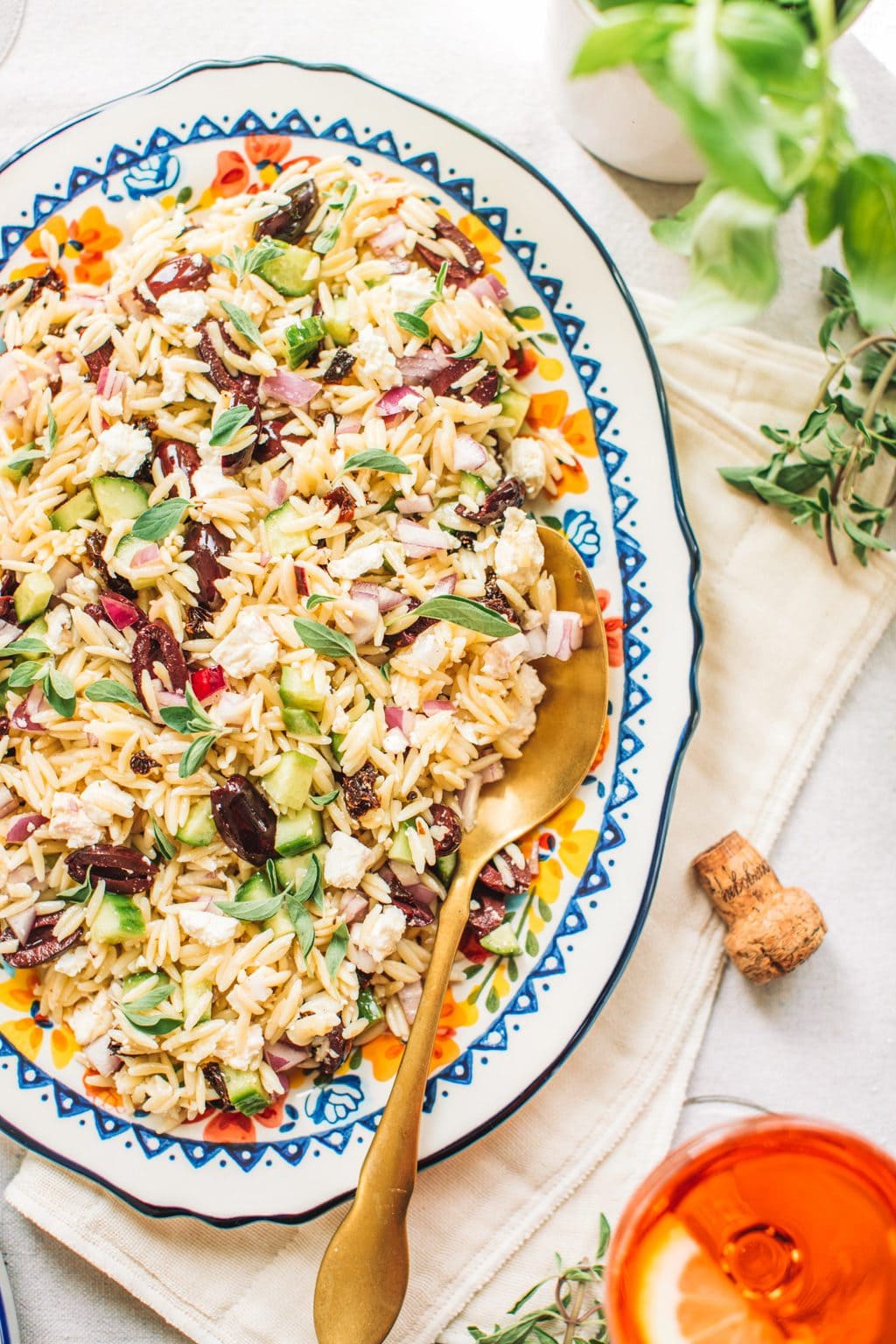 Top shot of orzo lemon salad with gold spoon on large oval serving dish.