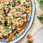 Top shot of orzo lemon salad with gold spoon on large oval serving dish.