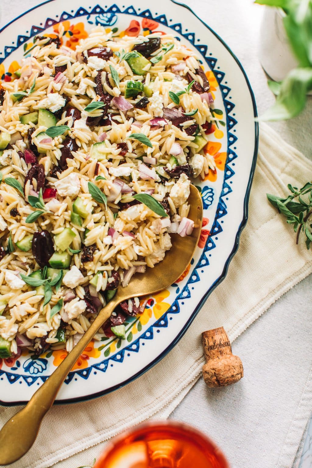 Top shot of orzo lemon salad with gold spoon on large oval serving dish.