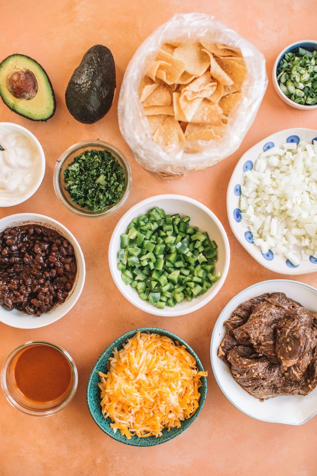 Bowls of sour cream, cilantro, black beans, enchilada sauce, steak, onions, green onions, chips and avocado.