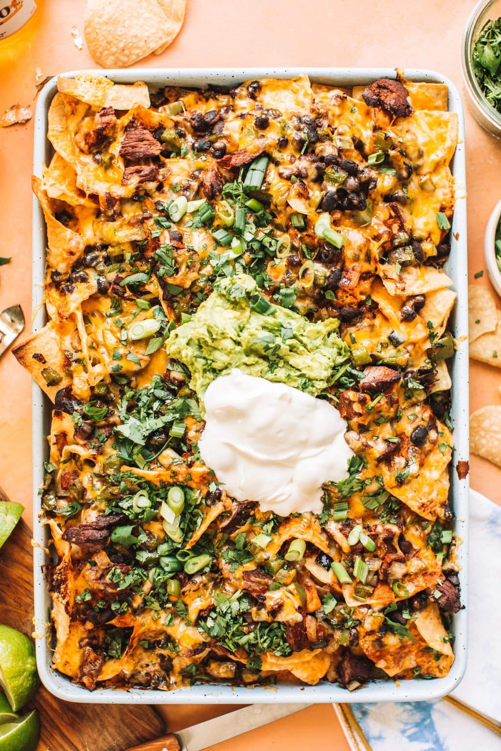 A sheet pan of steak fajita nachos topped with cilantro, green onions, guacamole and sour cream.