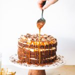 Woman holding spoon dripping caramel sauce onto banoffee cake.