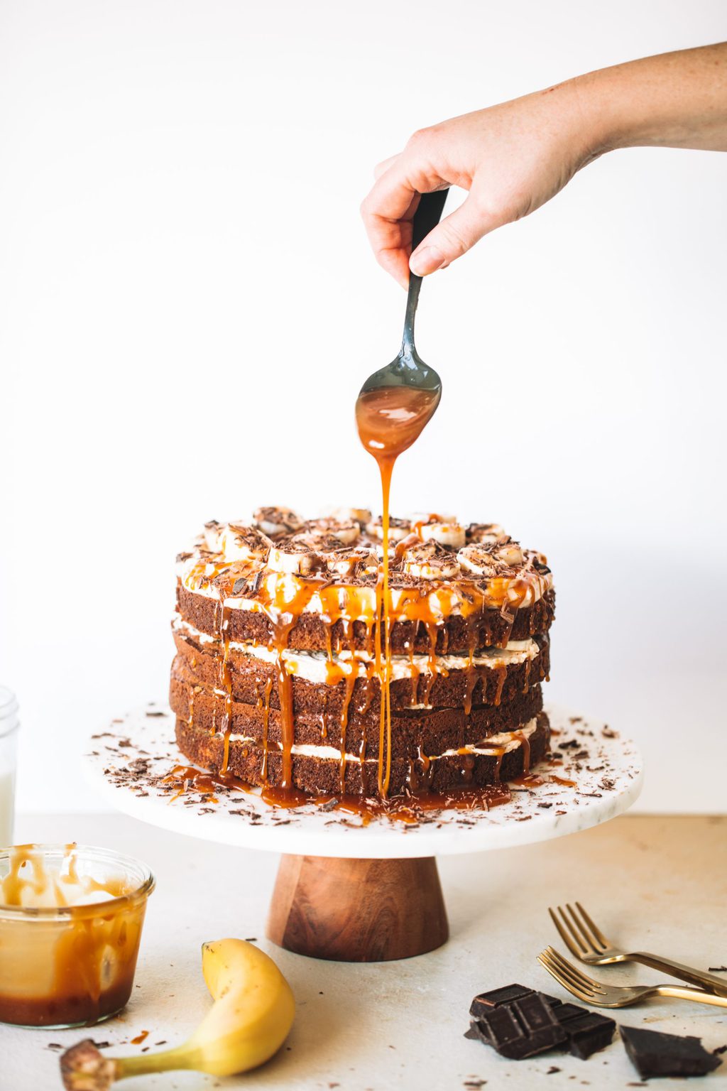 Woman holding spoon dripping caramel sauce onto banoffee cake.