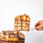 Slice of banana caramel cake being taken from whole cake off of cake stand.