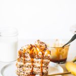 Slice of banana and caramel cake on white plate next to gold fork.