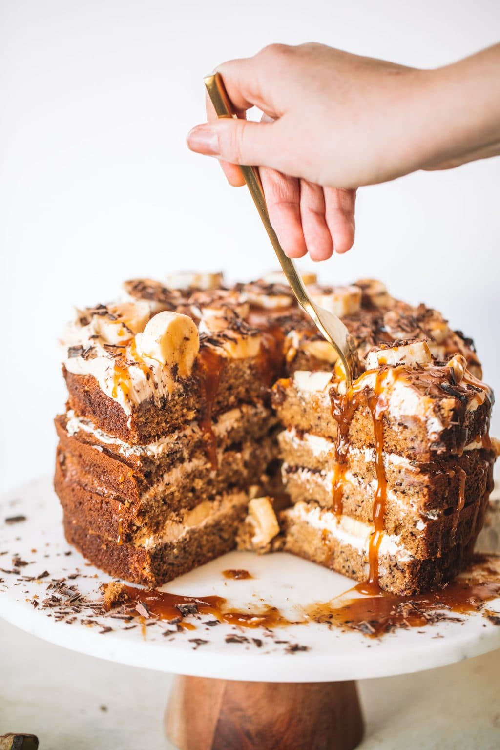 Woman putting fork into banana caramel cake with slices cut out.