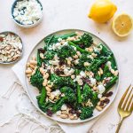 Top shot of broccoli salad with dried cranberries and white beans on plate next to gold fork and sliced lemon.