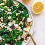 Top shot of broccolini salad with dried cranberries and white beans on plate next to gold fork and sliced lemon.