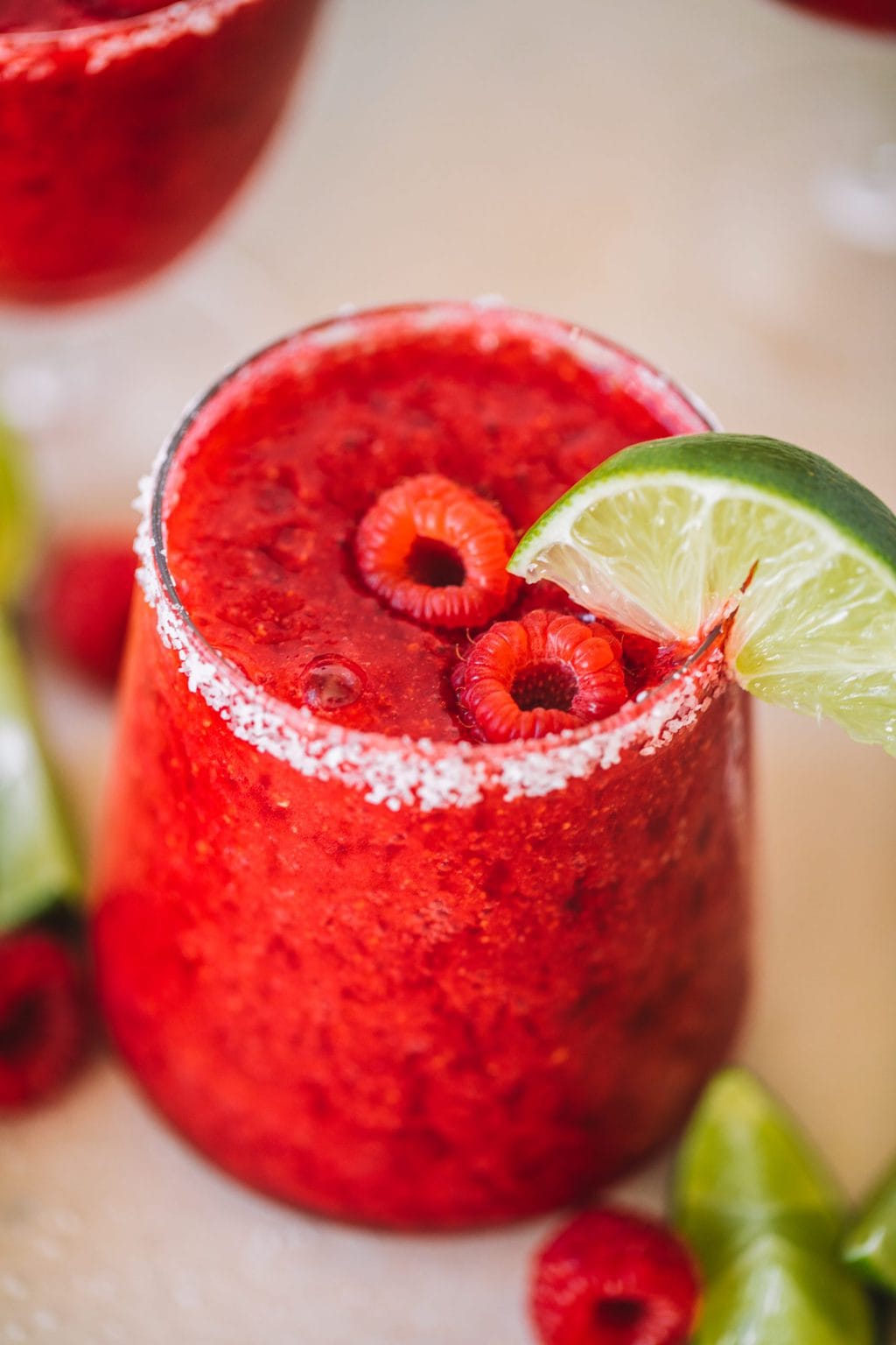 Frozen raspberry margarita with fresh raspberries and a lime wedge. 