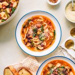 Top shot of two bowls of minestrone soup next to slices of toast.