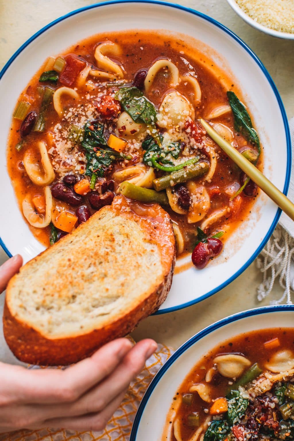 Dipping toast into Minestrone Soup Olive Garden Style in white bowl.