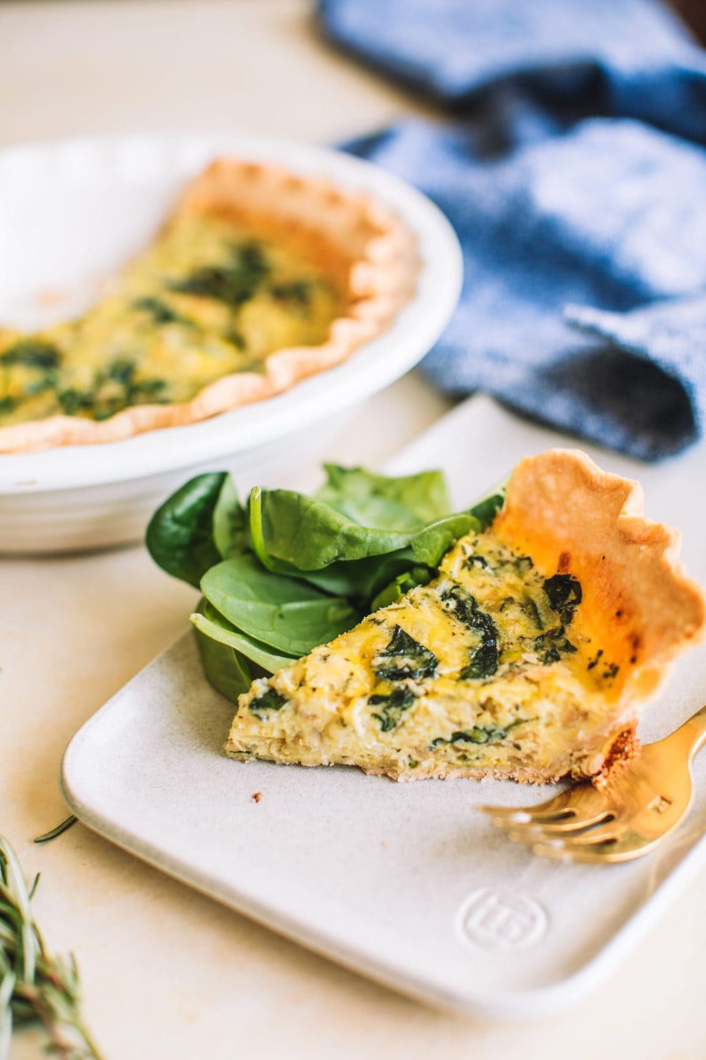 slice of spinach quiche on a plate with fresh spinach and fork