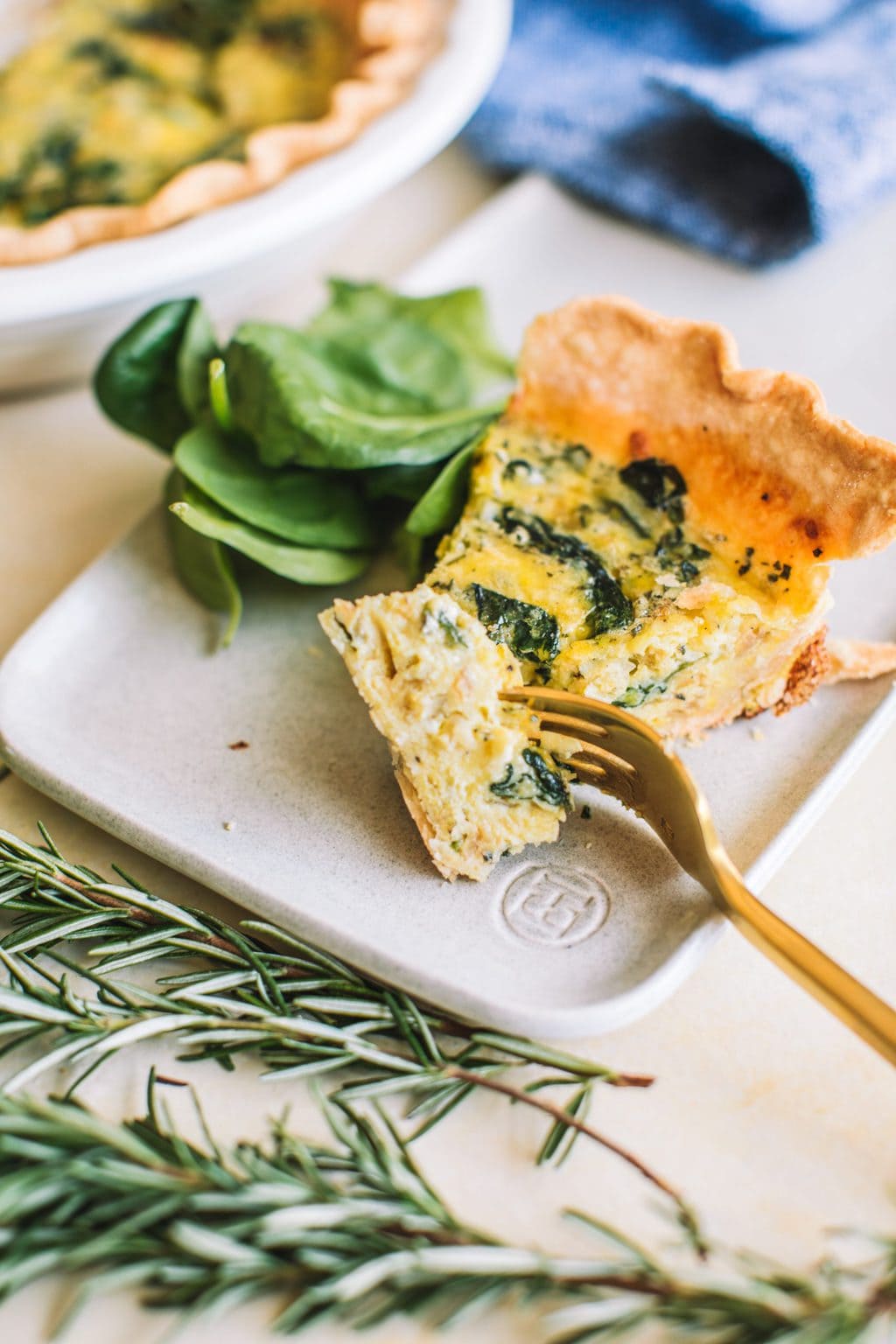 slice of spinach quiche on a plate with fresh spinach and fork