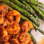 Close up shot of cooked shrimp next to asparagus on plate.