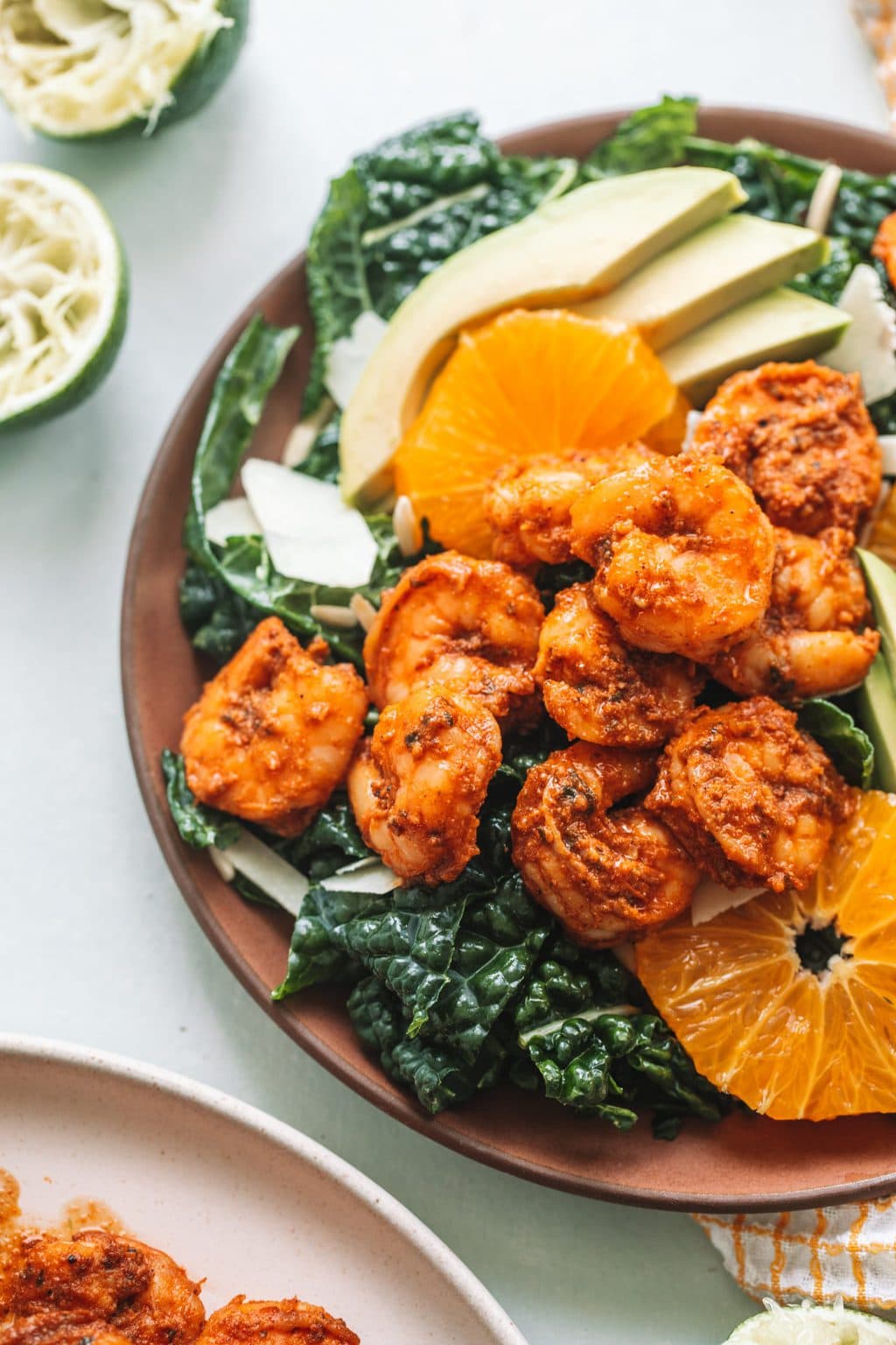 Seafood on bed of lettuce with avocados and orange slices on red plate.